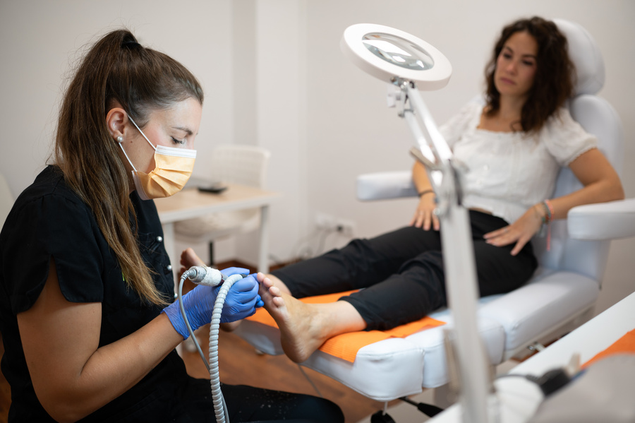 Podiatrist using electric file treating patient's foot in clinic