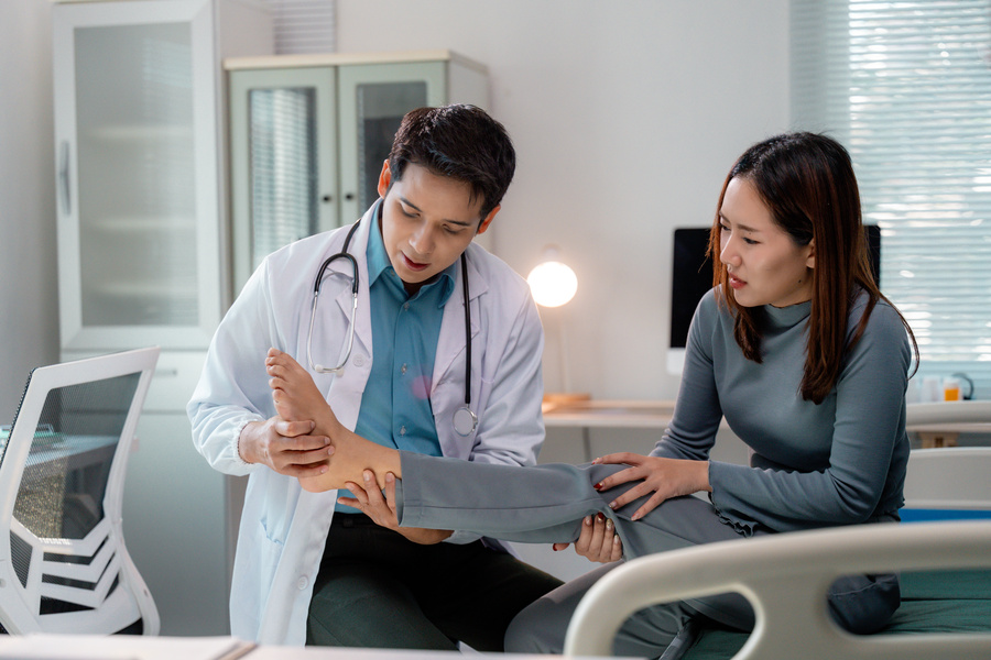 Doctor examining injured foot of female patient with diabeties sitting on hospital bed